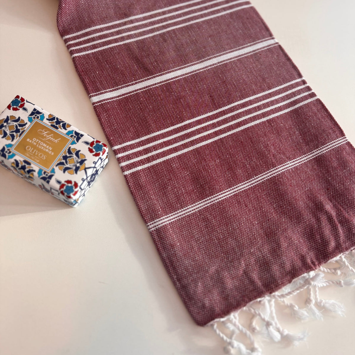 Burgundy CLASSIC Turkish Towel with white stripes on a white surface, next to a bar of soap.