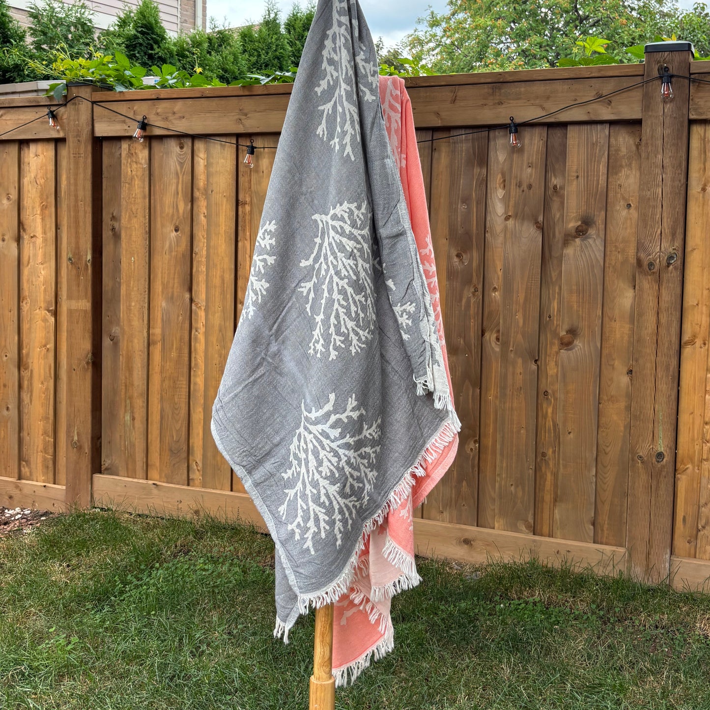 Grey Turkish towel with white coral patterns draped over a wooden structure outdoors