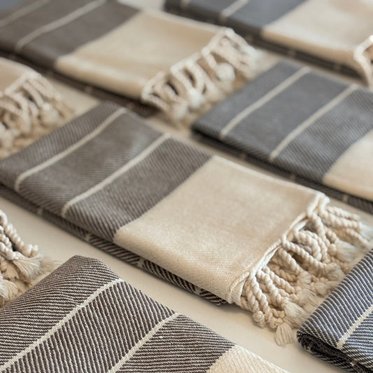 Set of grey and brown striped mini Turkish hand towels with tassels on a white surface
