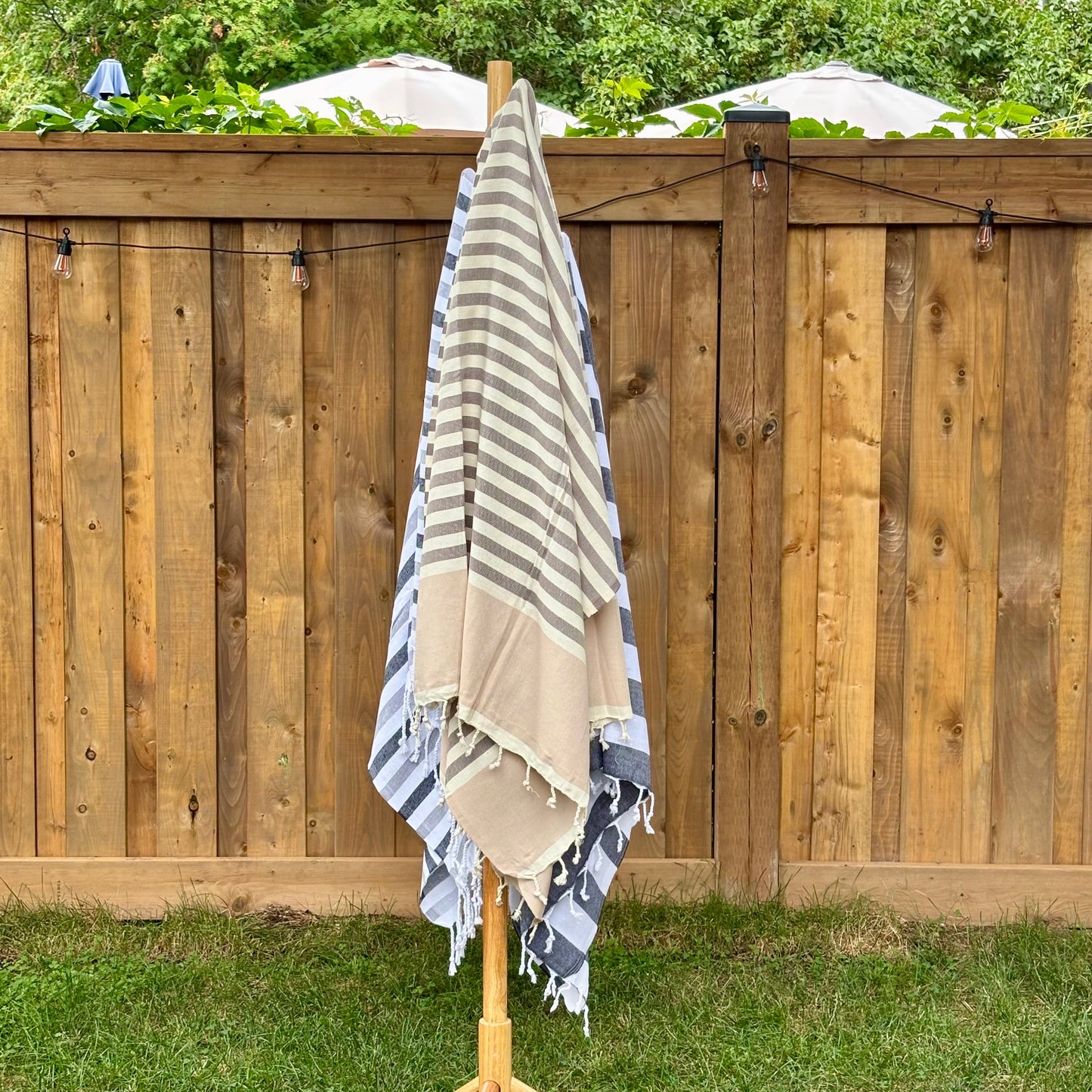 Brown and beige striped towel hanging on a wooden rack against a wooden fence with greenery.