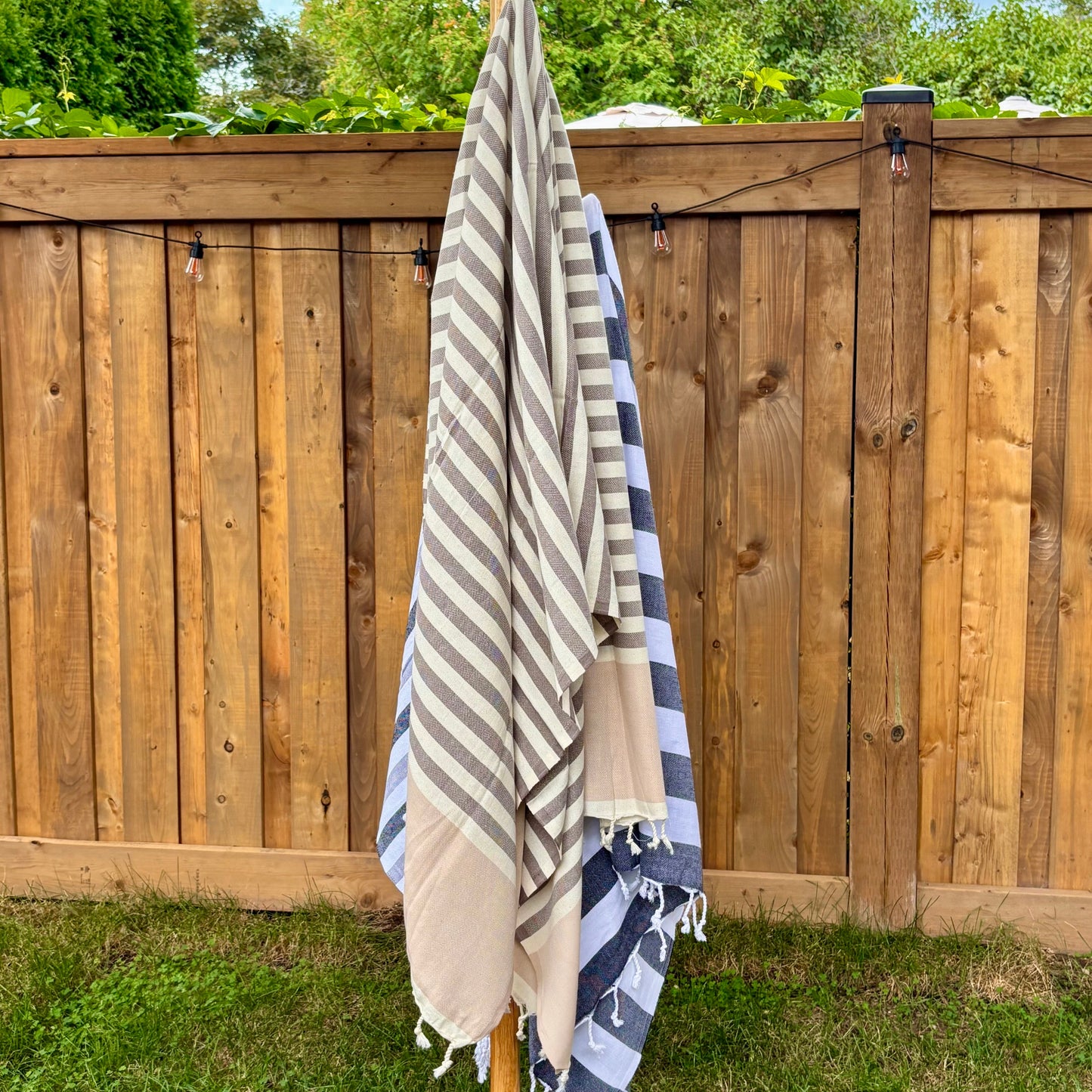 Brown and beige striped towel hanging on a wooden rack with a wooden fence and trees in the background.