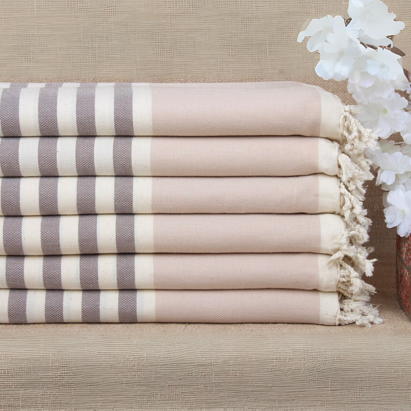 Stack of striped Turkish bath and beach towels with tassels on a light brown surface