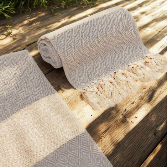 Rolled ISTANBUL Turkish Towel with diamond weave and tassels on rustic wooden deck.