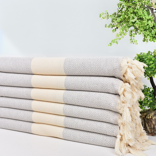 Stack of ISTANBUL Turkish Towels with beige and grey diamond pattern and hand-knotted fringes.