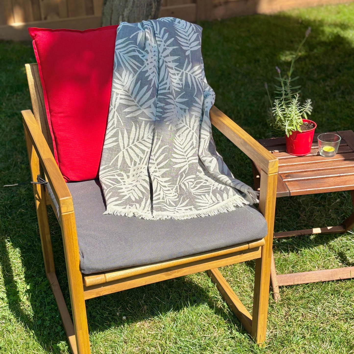 Wooden chair with red pillow, grey cushion, and leaf-patterned Turkish towel throw blanket on grass
