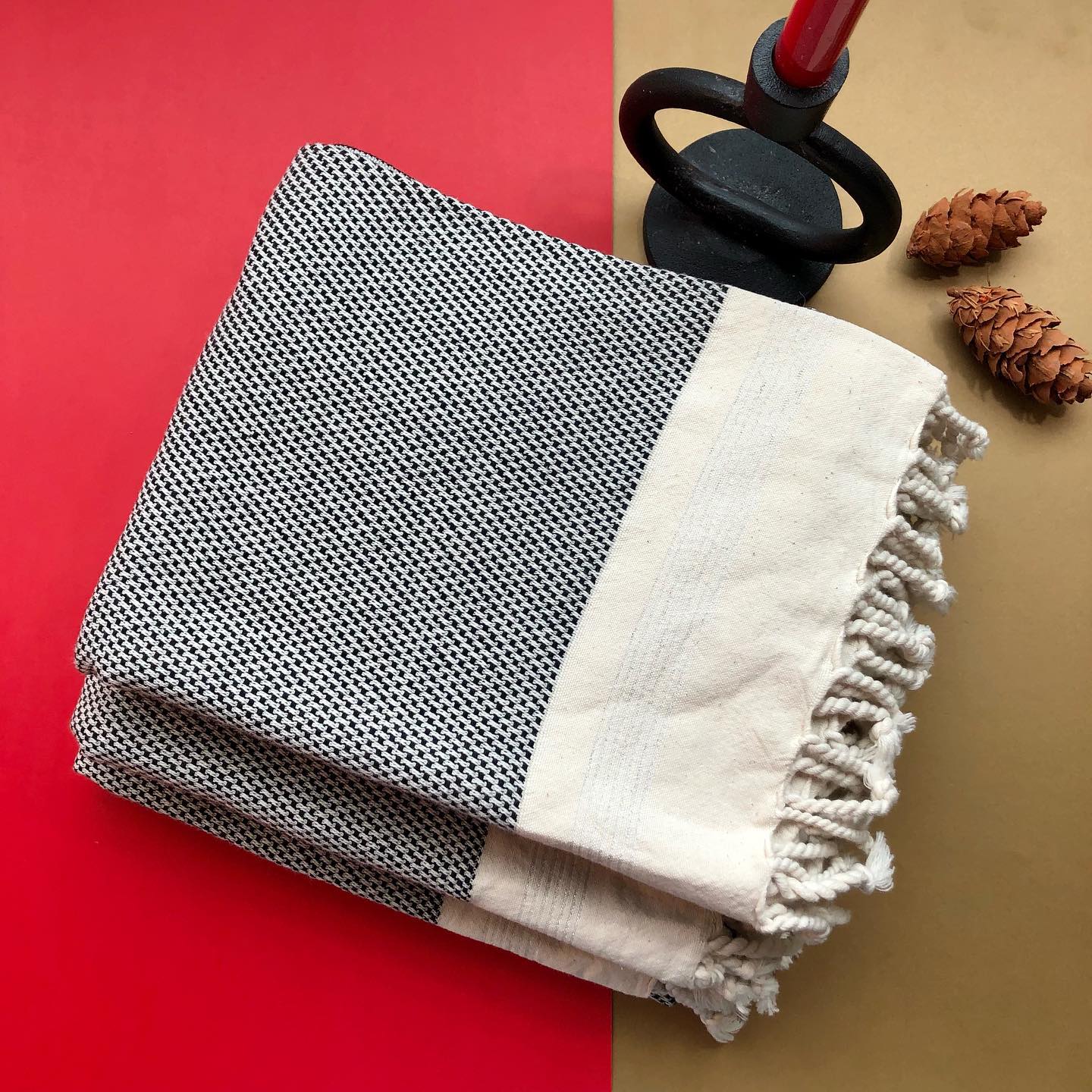MIDNIGHT double-sided Turkish towel with black and white patterns, folded on a red and beige background, accompanied by a festive red candle in a black candle holder and pine cones
