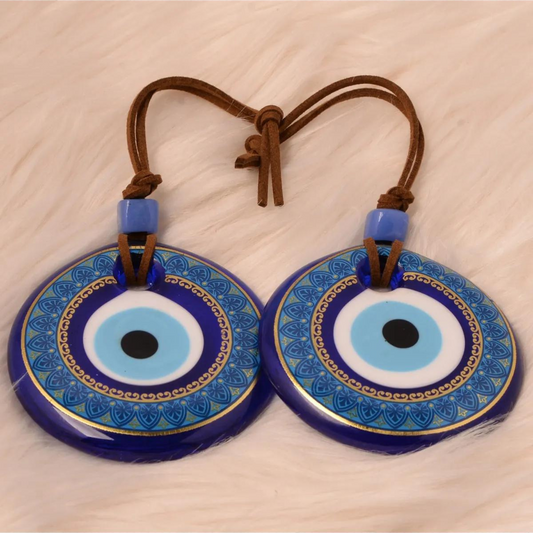 Two Nazar wall hangings with blue and gold designs, connected by a brown cord with a knot, placed on a plush white background