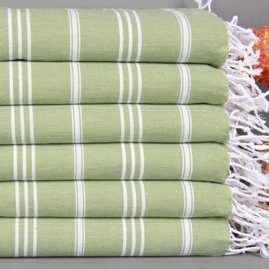 Stack of pistachio green and white striped Turkish hand and kitchen towels with fringes on a gray surface
