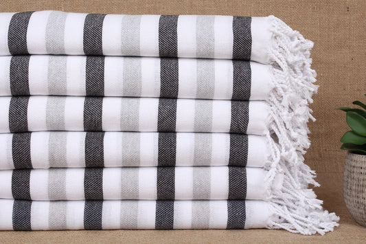 Stack of grey and white striped Turkish towels with fringes on a textured surface