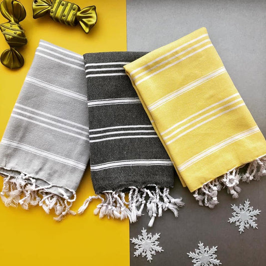 Three striped kitchen Turkish towels in grey, black, and yellow on a yellow and grey background with Christmas bows and snowflakes.