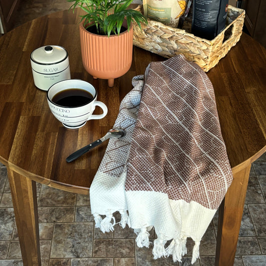 Coffee cup, plant, basket with coffee packages, and WALNUT Turkish Hand Towel draped over on a wooden kitchen table.