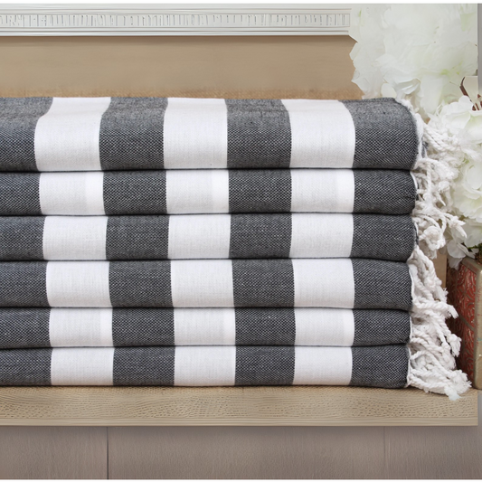 Stack of black and white striped Turkish towels with tassels on a wooden surface.