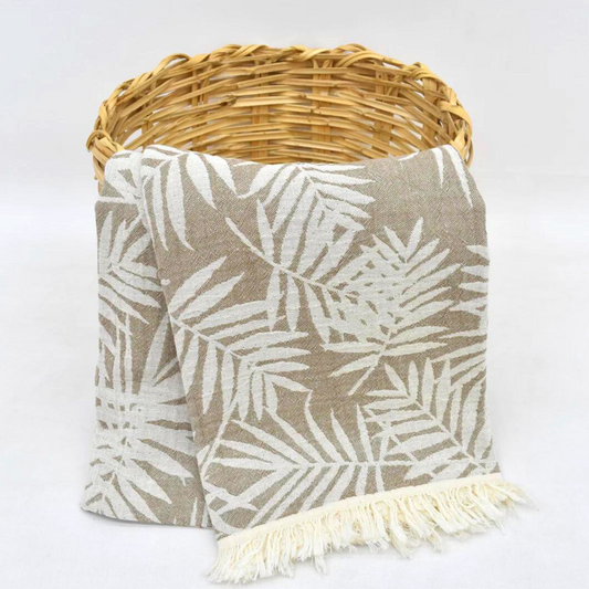 Brown Turkish towel with leaves pattern hanging from a basket, used as a cozy throw blanket