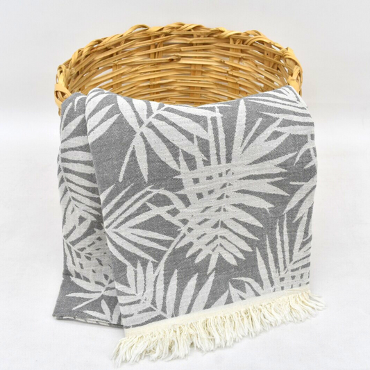 Grey Turkish towel with leaves pattern hanging from a basket as a cozy throw blanket