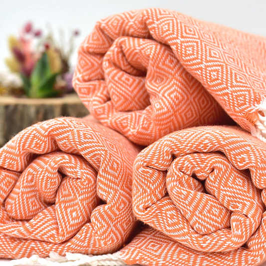 Rolled orange SULTAN Turkish towels with diamond weave pattern, made of soft cotton, perfect for bath, spa, or beach use.