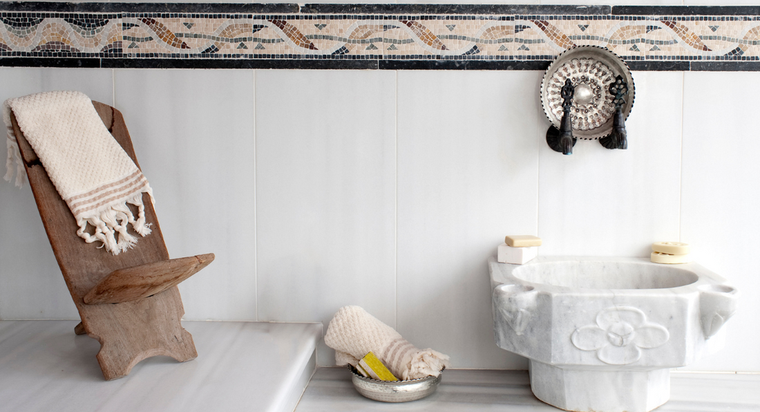 Traditional Turkish bath with marble sink, wooden chair, and Turkish towels. Includes olive oil soaps, highlighting the luxurious hammam experience.