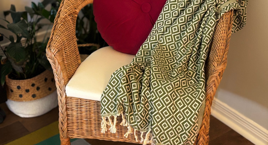 Thyme Peshtemal Towel in deep green draped on wicker chair with autumn pillow for seasonal home decor.