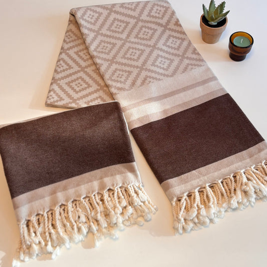 Brown and beige patterned Turkish towel with tassels on a light surface.