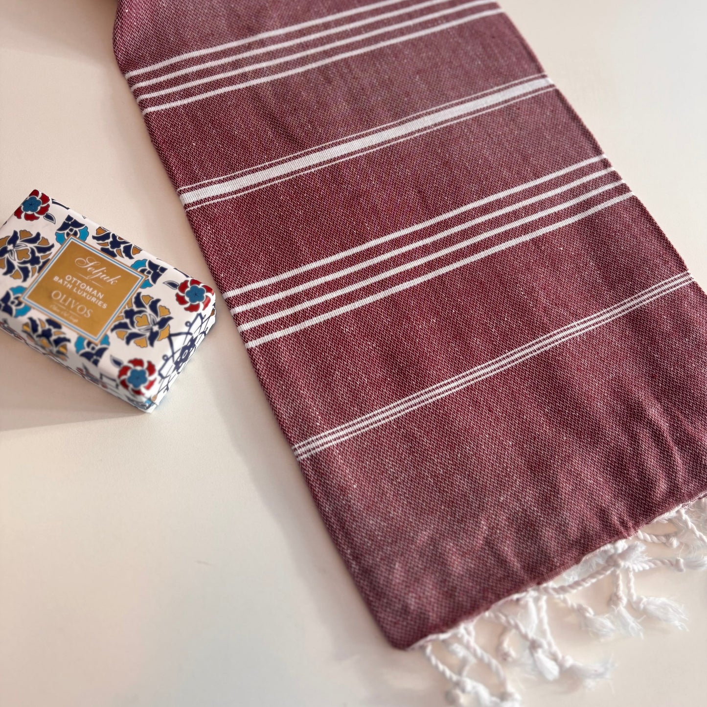 Burgundy CLASSIC Turkish Towel with white stripes on a white surface, next to a bar of soap.