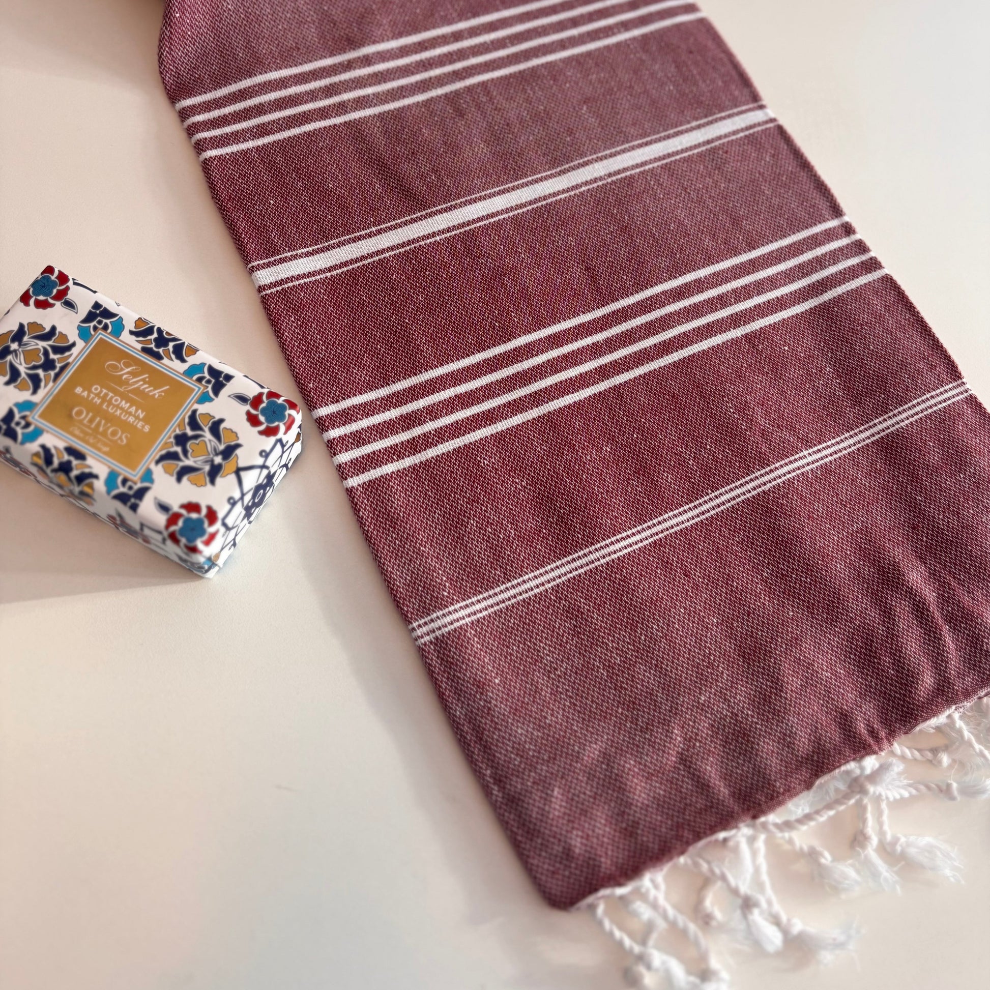 Burgundy CLASSIC Turkish Towel with white stripes on a white surface, next to a bar of soap.