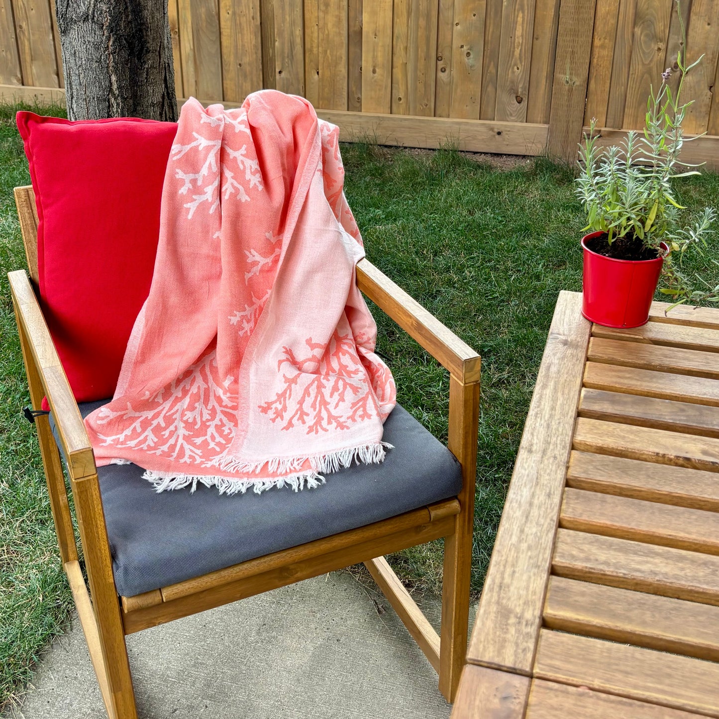 Chair with a pink coral reversible Turkish towel and red pillow on a patio with a wooden table and potted lavender.