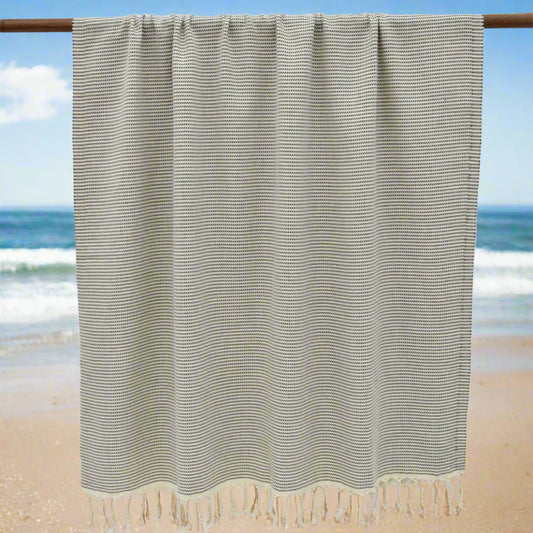 Textured beige Turkish towels with traditional hand-knotted fringes hanging on a wooden rod.