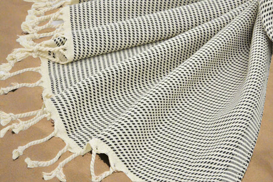 Black and beige patterned DUNES Turkish Towel with tassels on sandy beach