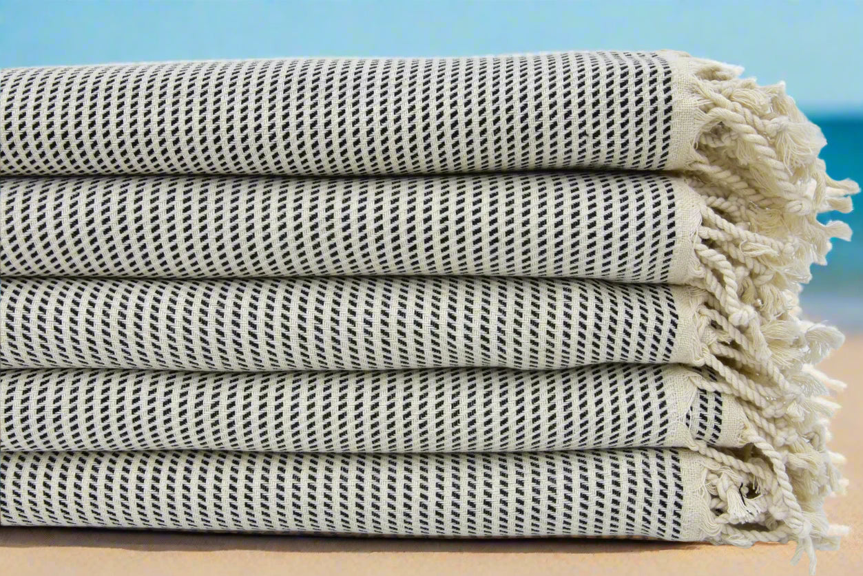 Stack of folded beige Turkish towels with traditional hand-knotted fringes on edges.