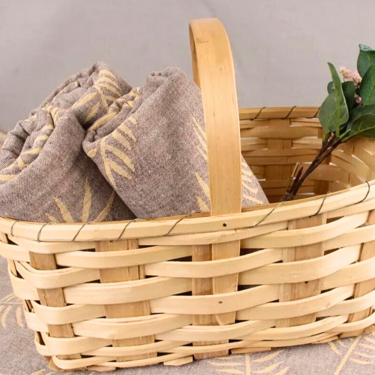FERN Turkish Towels folded in a light wooden basket, accented with green leaves and twigs