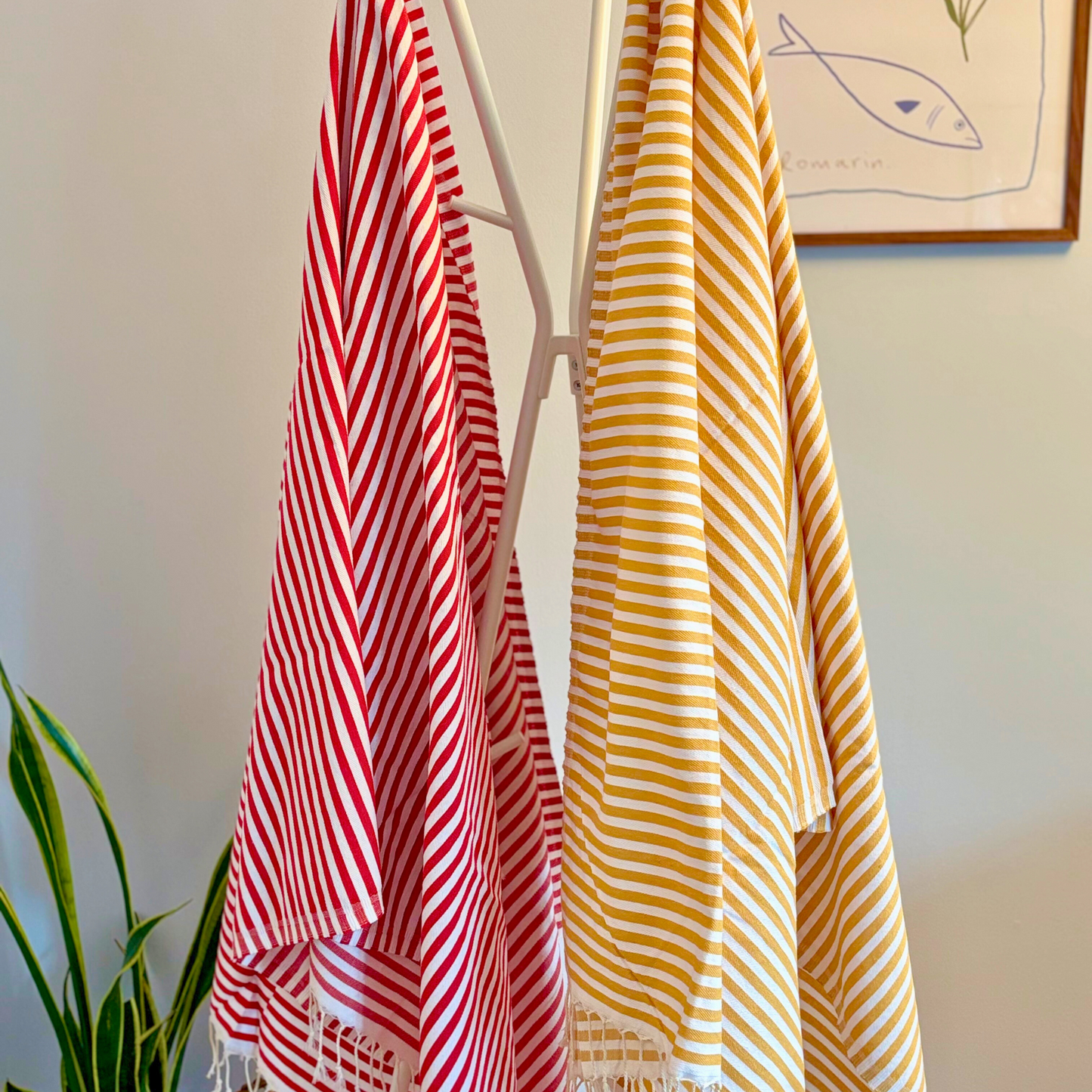 FUN Turkish Towels in wine red and mustard yellow with white stripes, displayed on a rack with hand-knotted fringes