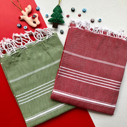 Two striped Turkish towels, one green and one red, on a red surface with Christmas decorations.