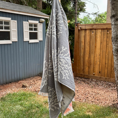 Grey Turkish towel with white coral patterns hanging outdoors against a wooden fence and blue shed.
