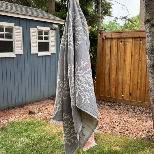 Grey Turkish towel with white coral patterns hanging outdoors against a wooden fence and blue shed.