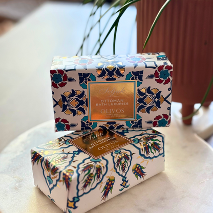 Two bars of HAMMAM Olive Oil Soap, one with a Seljuk design and the other with a Tulip pattern, arranged on a marble surface with a plant in the background, conveying a sense of luxury bath essentials