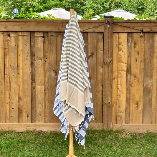 Brown and beige striped towel hanging on a wooden rack against a wooden fence with greenery.