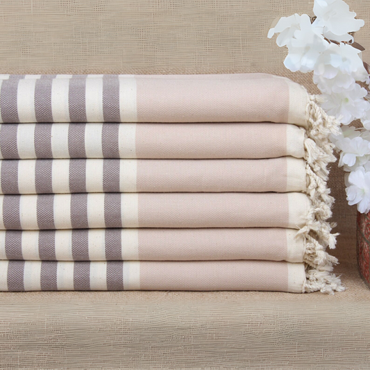 Stack of striped Turkish bath and beach towels with tassels on a light brown surface