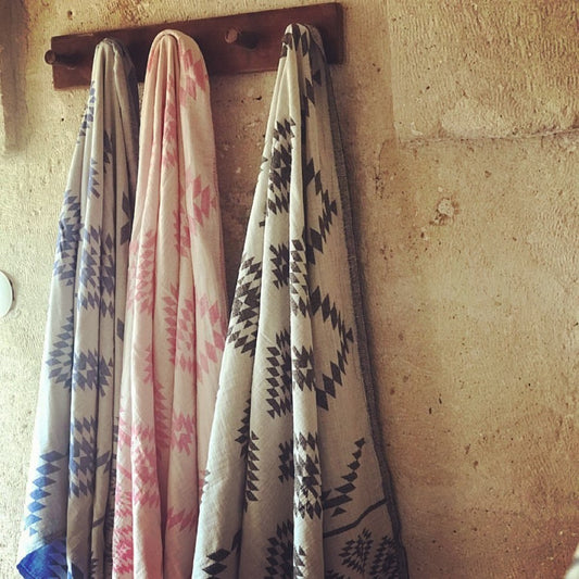 KILIM Double-Sided Turkish Towels in blue, pink, and black geometric patterns hanging on rustic wall hooks, ideal for bath or beach use.