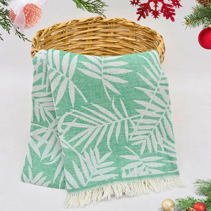 Green LEAVES Peshtemal Towel with white leaf pattern on a wicker basket against a light background with Christmas decorations.