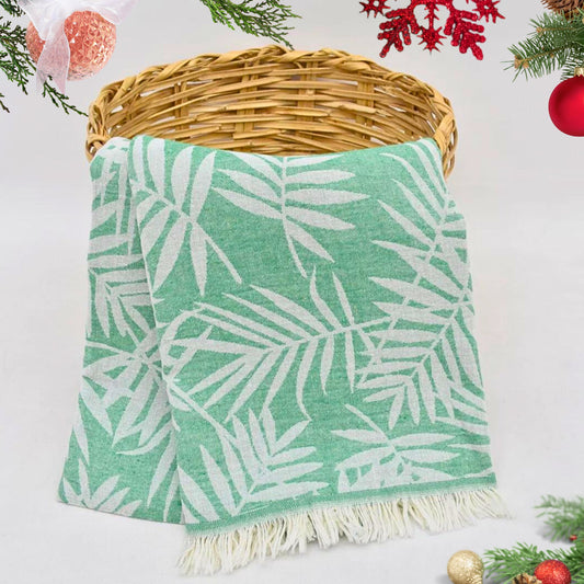 Green LEAVES Peshtemal Towel with white leaf pattern on a wicker basket against a light background with Christmas decorations.