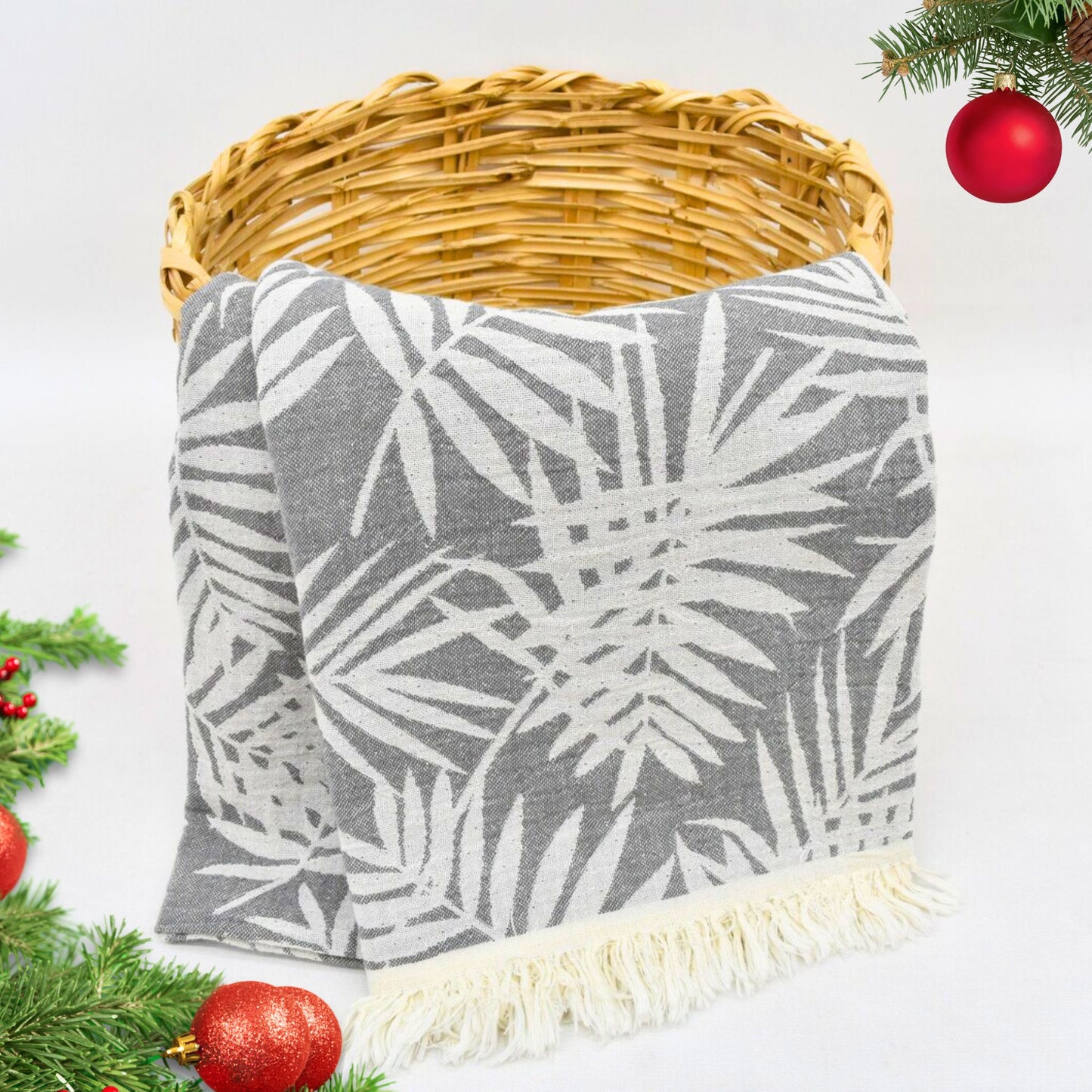 Gray leaf-patterned LEAVES Peshtemal Towel throw blanket with white fringe on a white background with Christmas decorations.