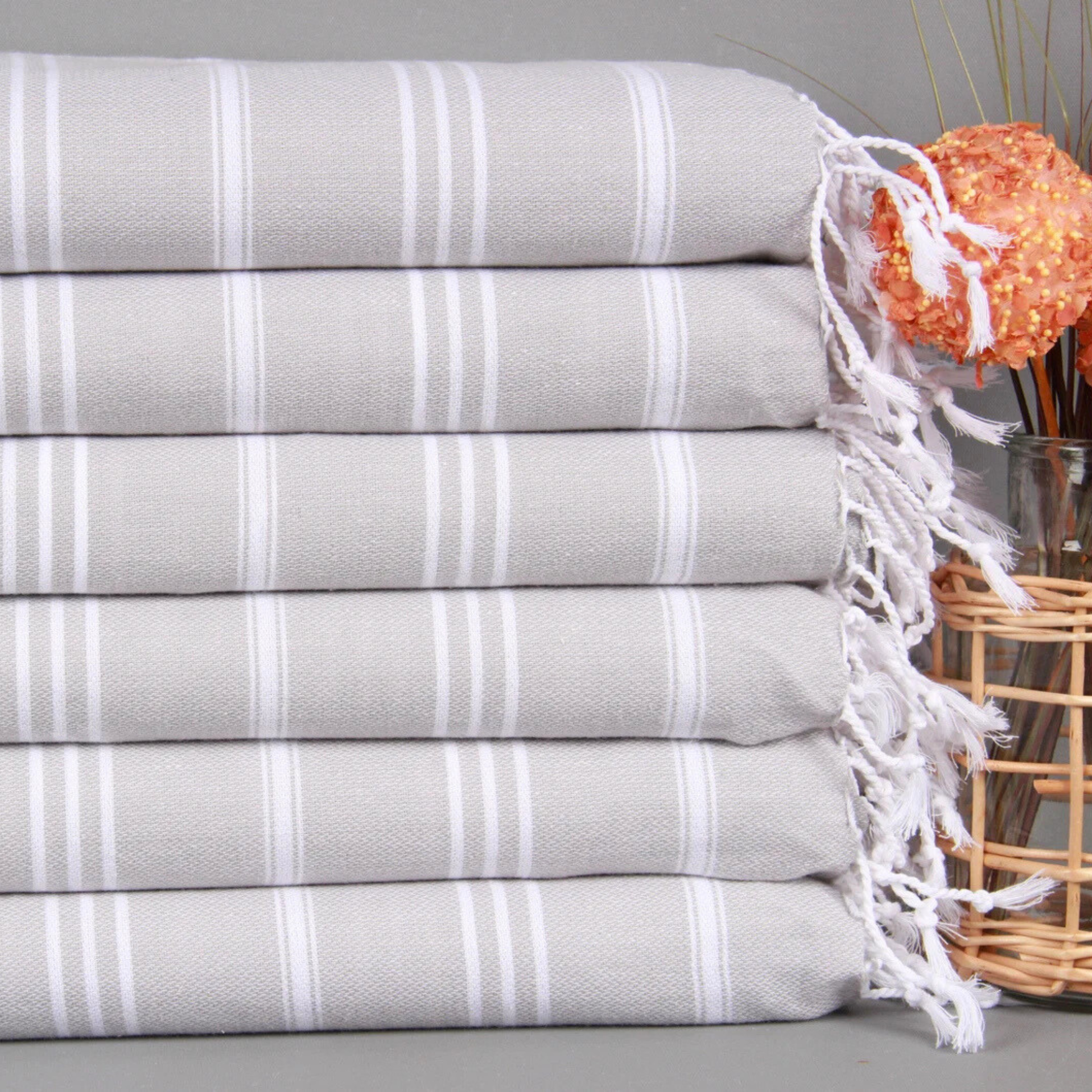 Stack of grey striped Turkish hand and kitchen towels with white fringe next to orange dry flowers.