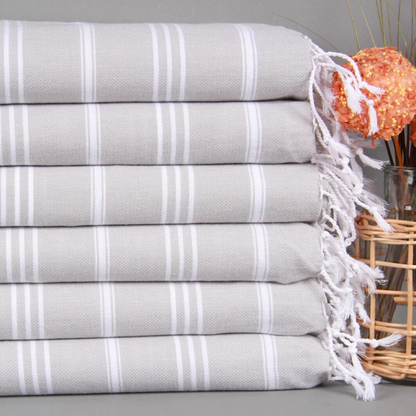 Stack of grey striped Turkish hand and kitchen towels with white fringe next to orange dry flowers.