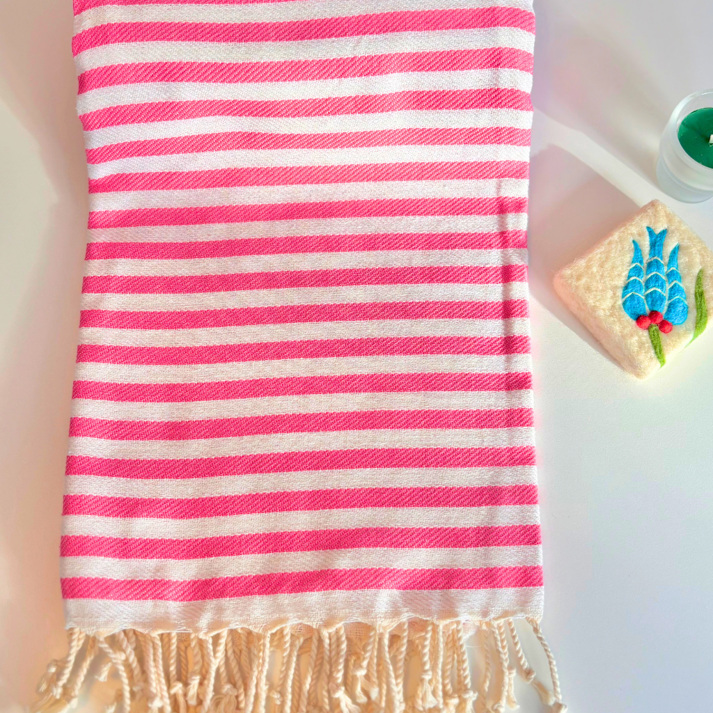 Striped towel with pink and white stripes on a light background next to felted soap and candle
