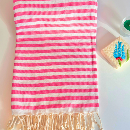 Striped towel with pink and white stripes on a light background next to felted soap and candle