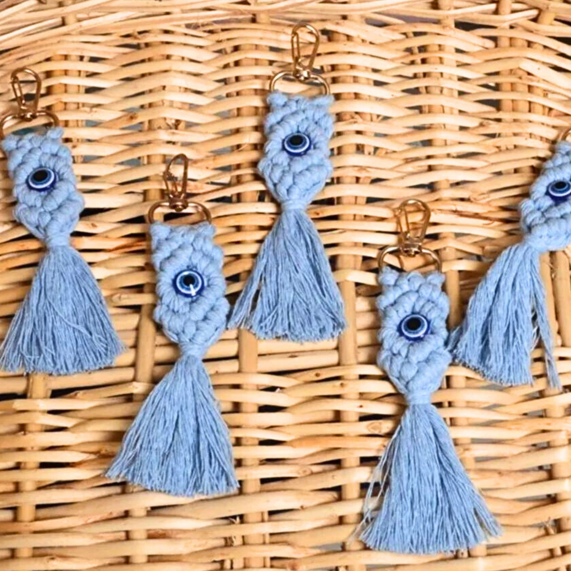 Blue macrome evil eye keychains with tassels on a wicker background
