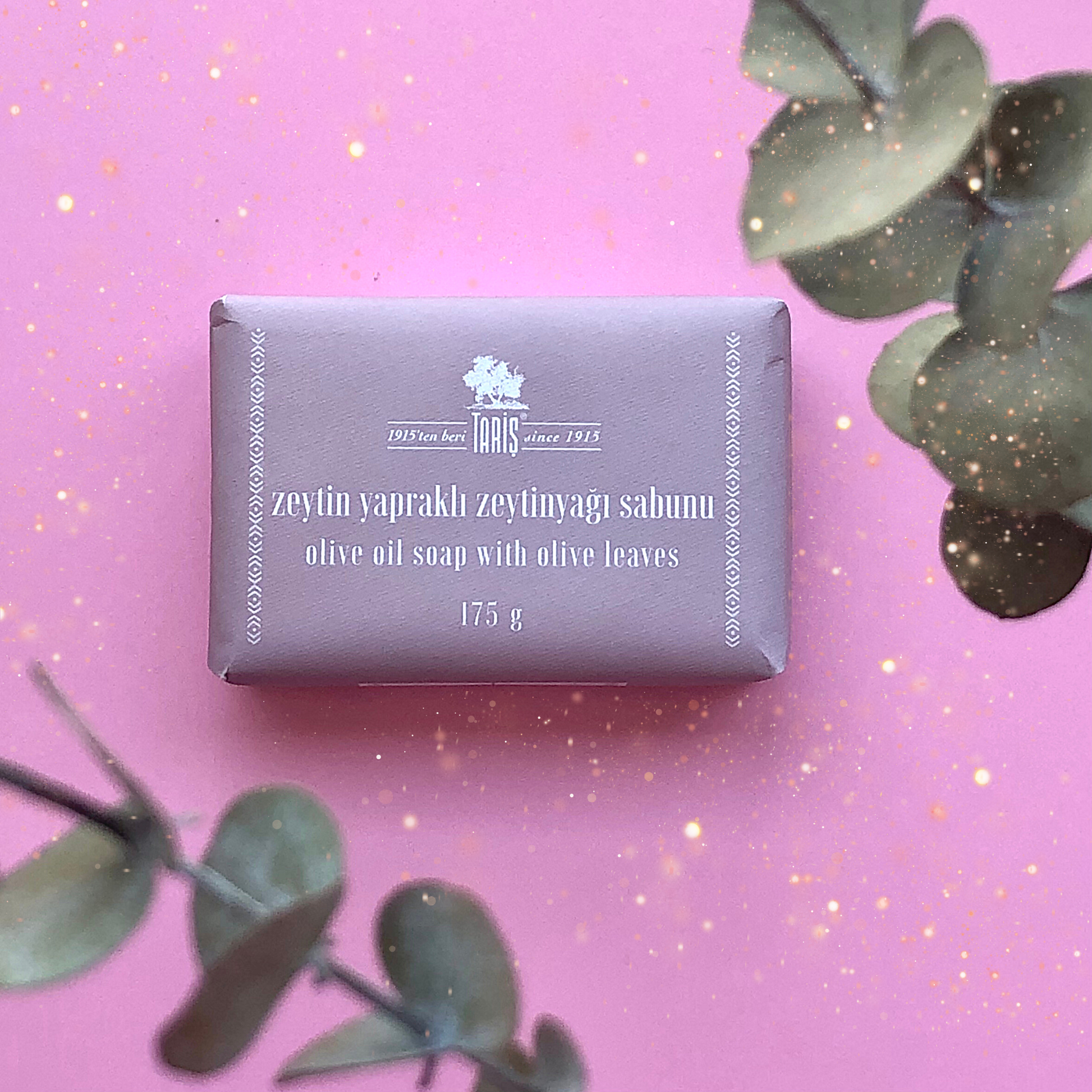 Bar of OLIVE LEAVES Soap with packaging on a pink background with eucalyptus leaves and festive sparkles.