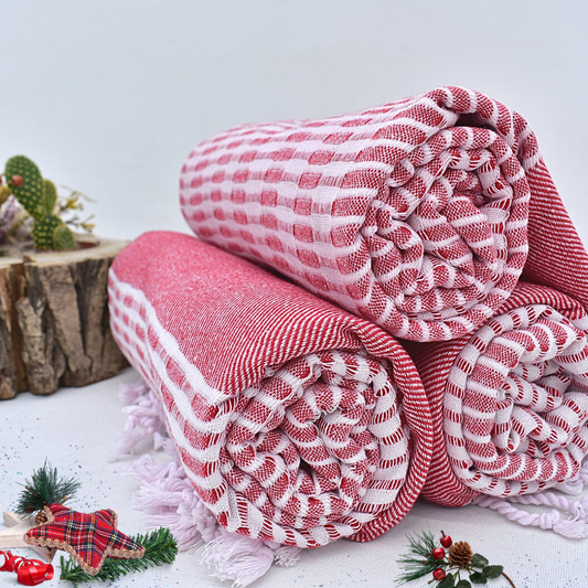 Rolled red and white checkered Turkish towels with festive decorations on a white backdrop