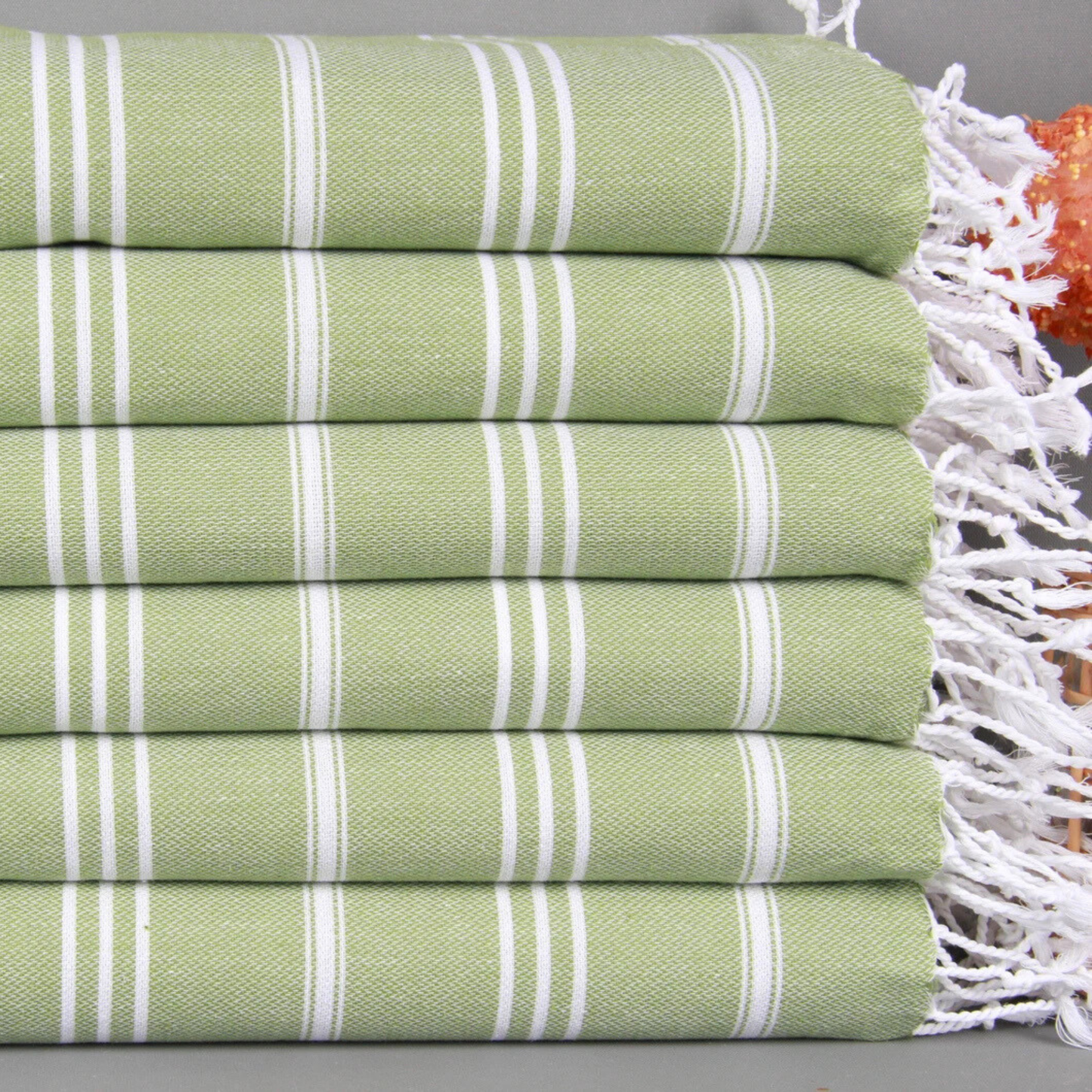 Stack of pistachio green and white striped Turkish hand and kitchen towels with fringes on a gray surface