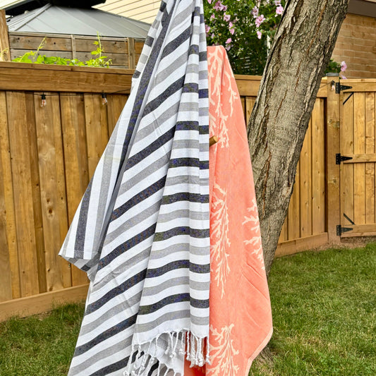 Two Turkish beach towels, one striped and one pink, hanging on a wooden stand outdoors.