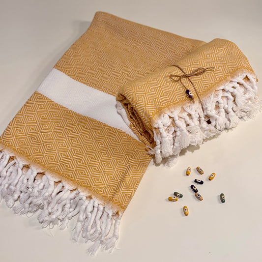 Mustard yellow Turkish towel with diamond patterns and white fringe on a light background